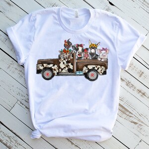 May include: White t-shirt with a graphic of a brown and white pickup truck with a cow, pig, donkey, and chickens in the bed.