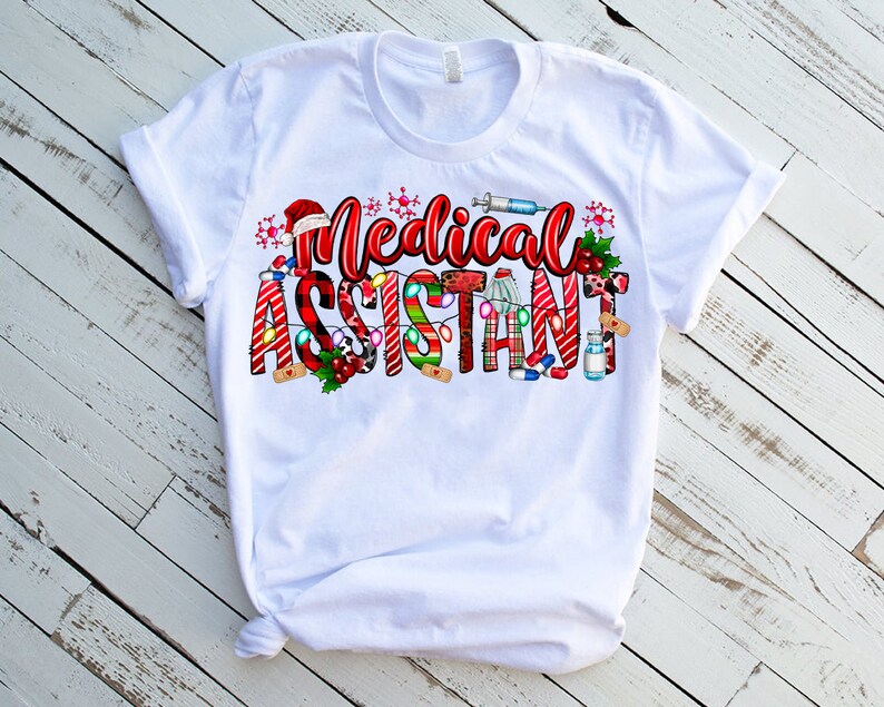 Puede incluir: Camiseta blanca con un dise&ntilde;o navide&ntilde;o que dice "Asistente M&eacute;dico". El dise&ntilde;o incluye bastones de caramelo, luces y s&iacute;mbolos m&eacute;dicos.