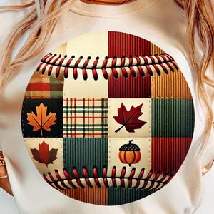Puede incluir: Sudadera color crema con un diseño de béisbol. El diseño presenta un patrón de patchwork con hojas de arce, cuadros y una bellota en tonos rojos, naranjas, verdes y marrones. El béisbol tiene costuras rojas.