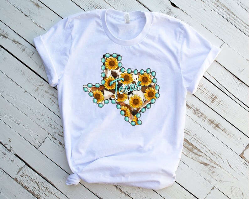Puede incluir: Camiseta blanca con un gr&aacute;fico del estado de Texas delineado con cuentas turquesa y relleno con un patr&oacute;n de estampado de vaca y girasoles.