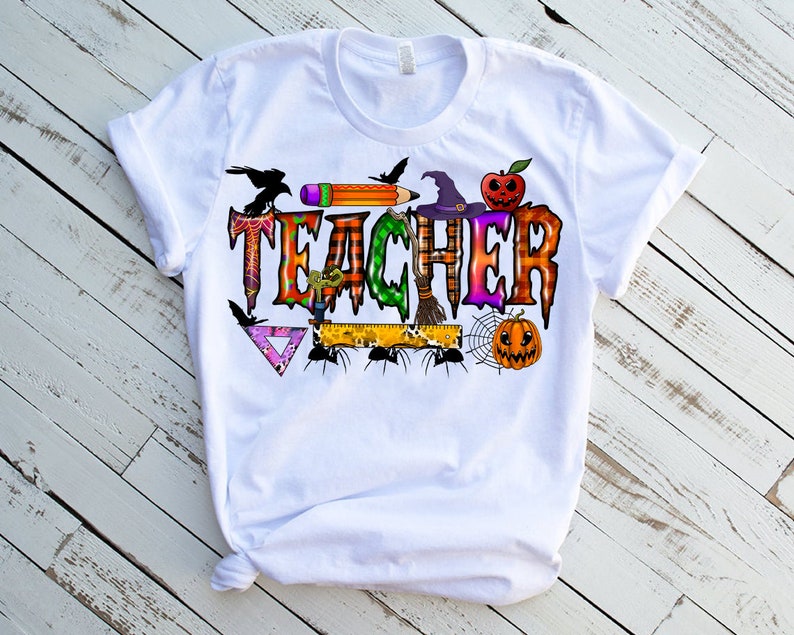 May include: White t-shirt with a Halloween-themed "Teacher" graphic. The graphic features a witch's hat, a spider web, a pumpkin, a pencil, a ruler, and a crow.