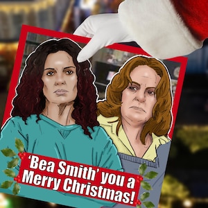 May include: A Christmas card featuring illustrations of two women. The card has a red border and the text "'Bea Smith' you a Merry Christmas!" is displayed on a teal banner with holly accents. The card is held by a gloved hand.