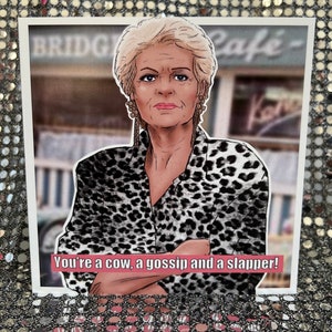 May include: A humorous greeting card featuring a cartoon illustration of a woman with blonde hair wearing a leopard print shirt. The text on the card reads "You're a cow, a gossip and a slapper!"