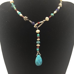 Pode incluir: Um colar de contas turquesa, branco, dourado e prateado com um grande pingente de gota turquesa.