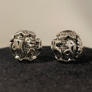 May include: Two silver beads with intricate designs, each bead is round and has a textured surface.