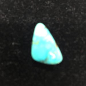 Puede incluir: Una piedra preciosa turquesa en cabujón con una matriz blanca. La piedra tiene forma de lágrima y una superficie lisa y pulida.