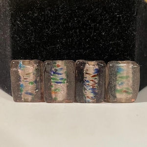 May include: Four rectangular glass beads with a clear background and colorful, iridescent, and metallic flecks. The beads are arranged in a row.
