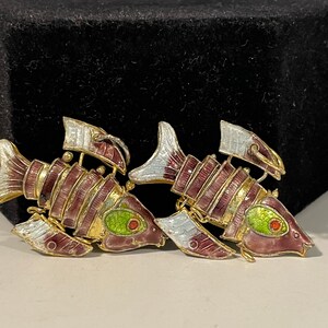 May include: Two gold-toned fish brooches with red, white, and green enamel. The fish have a detailed design with gold accents.