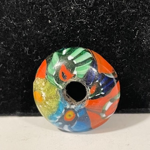 May include: A colourful glass bead with a hole in the centre. The bead is decorated with swirls of red, green, blue, yellow, and white.
