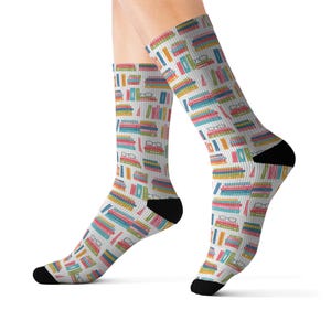 May include: A pair of knee-high socks with a white background and a colorful pattern of books and eyeglasses. The books are in various colors, including red, blue, yellow, and green. The socks have black heels and toes.