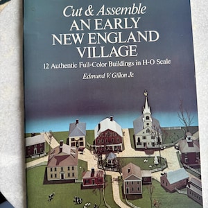 May include: A book titled "Cut & Assemble AN EARLY NEW ENGLAND VILLAGE" with a cover illustration of a village scene. The book features 12 full-color buildings in H-O scale. The author's name, Edmund V. Gillon Jr., is also visible.
