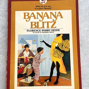May include: A book cover with a yellow banana character wearing a banana costume. The book title is "Banana Blitz" by Florence Parry Heide, author of "Banana Twist".