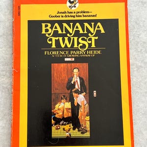 May include: A vintage paperback book titled "Banana Twist" by Florence Parry Heide. The cover features a black background with yellow text and an illustration of three people. The book has an orange border and the text "A BANTAM-SKYLARK BOOK".