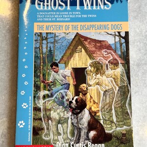 May include: A book cover with a blue background and the title "Ghost Twins: The Mystery of the Disappearing Dogs" in white text. The cover features an illustration of two children and a dog standing in front of a dog house in a forest.