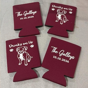 May include: Four maroon foam can coolers. Two feature the white text The Galloys and 10.10.2026. The other two feature the white text Drinks on Us, paw prints, and a line drawing of a dog. The items are arranged in a two-by-two grid pattern.
