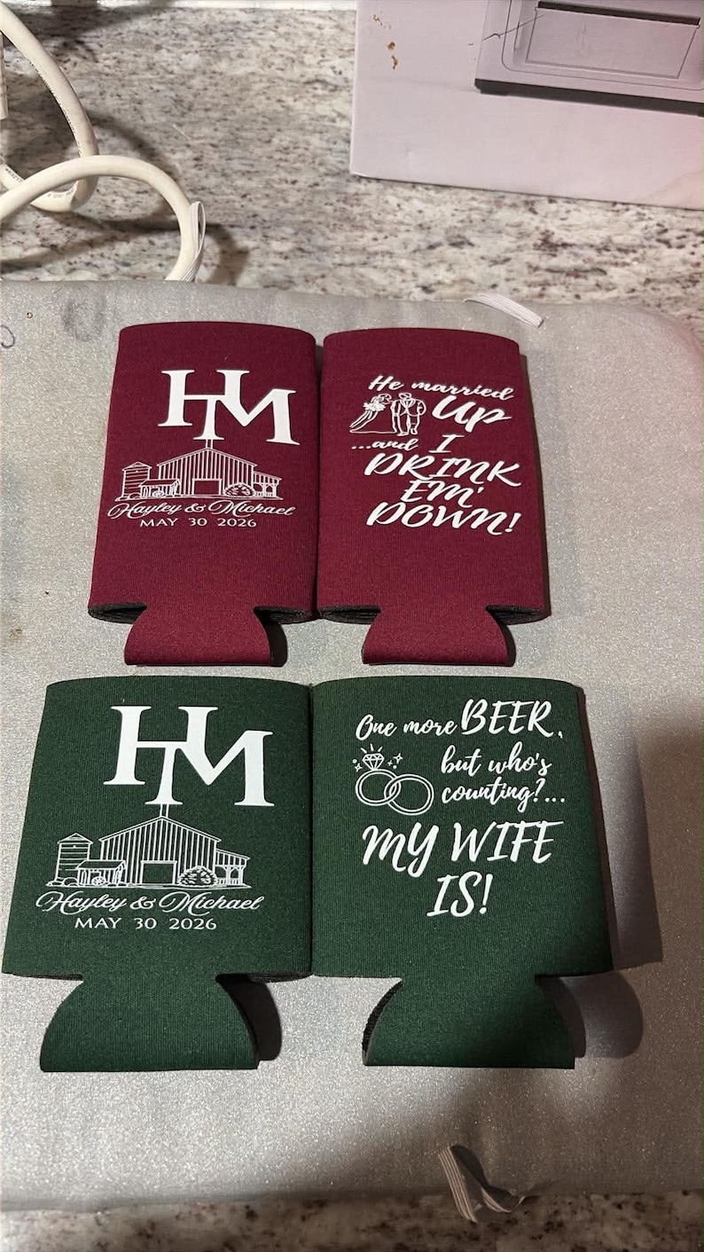 May include: Two burgundy and two dark green foam can coolers. The burgundy ones feature white text reading HM, a barn illustration, and Hayley & Michael MAY 30 2026, or He married up and I DRINK EM DOWN. The green ones feature the same HM design or One more BEER, but who's counting? my WIFE IS!