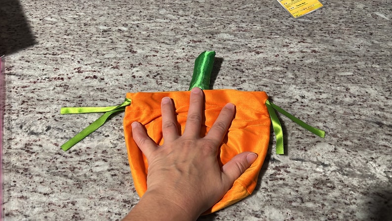 Pu&ograve; includere: Sacchetto a cordoncino di velluto arancione a forma di zucca con lacci di nastro verde e uno stelo di feltro verde.