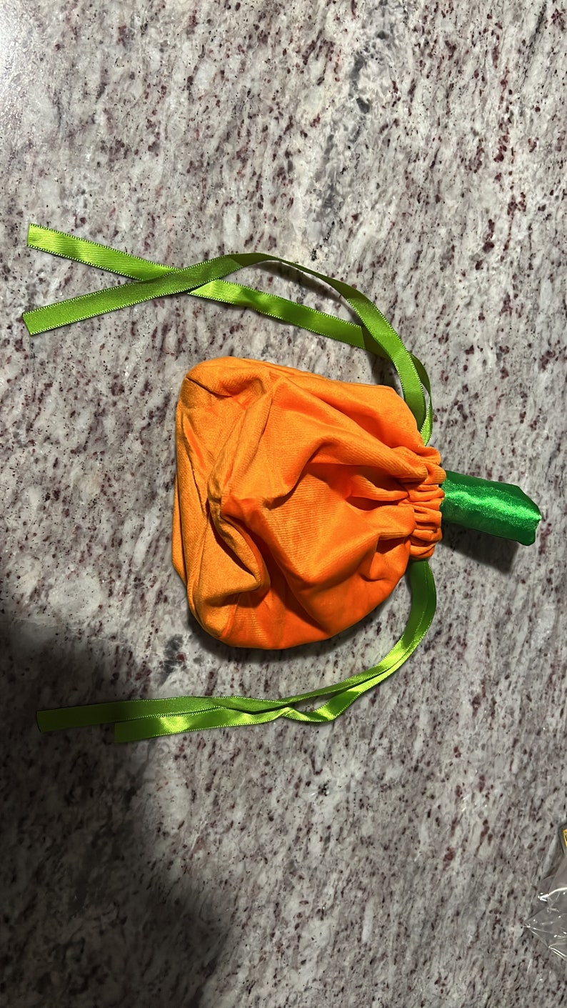 Pu&ograve; includere: Sacchetto a cordoncino in velluto arancione a forma di zucca con lacci in nastro verde.
