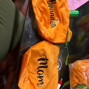 Pu&ograve; includere: Due sacchetti di velluto arancione a forma di zucca con manici in nastro verde. I sacchetti sono personalizzati con i nomi "Brandon" e "Mamma".