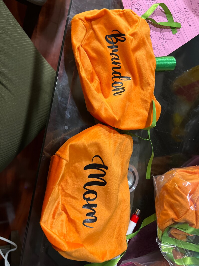 Pu&ograve; includere: Due sacchetti di velluto arancione a forma di zucca con manici in nastro verde. I sacchetti sono personalizzati con i nomi "Brandon" e "Mamma".