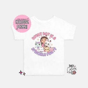 May include: White t-shirt with a pink and purple design featuring a girl and several cats. The text "Every Day Is A Sprinkle Party" is written in a pink and purple font.