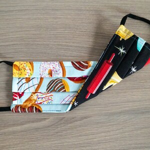 May include: A reusable face mask with a blue and white donut pattern on one side and a black fabric with a red rolling pin and white stars on the other side.