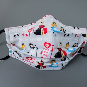 May include: A white face mask with a repeating pattern of Alice in Wonderland characters, including the Queen of Hearts, Alice, and the Mad Hatter. The text "I'll ask the questions, silence!" is repeated on the mask.