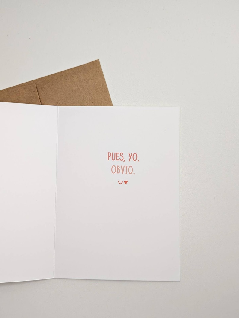 May include: A white card with the text "Pues, yo. Obvio." in pink. The card is folded in half and has a brown envelope behind it.