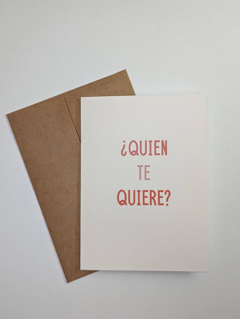 May include: A white card with a brown envelope. The card has the text "&iquest;QUIEN TE QUIERE?" in red.