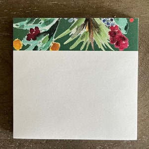 May include: A white rectangular notepad with a decorative top border. The border features a watercolor design of green leaves, red berries, and orange accents. The notepad is blank, offering space for notes or messages.