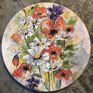 May include: A round ceramic plate with a watercolor painting of red poppies, white daisies, and purple flowers. The flowers are painted in a loose, impressionistic style.