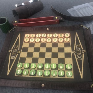 May include: A brown leather-bound chessboard with a black and white checkered playing surface. The board is rolled up and has a gold inscription that reads "RUSTIGO" on both sides. The board is accompanied by green and brown chess pieces.