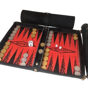 May include: Backgammon set with a red and black playing surface, featuring the word "RUSTIGO". Includes dice, game pieces, and a black carrying case. The set is open, displaying the game board and accessories.