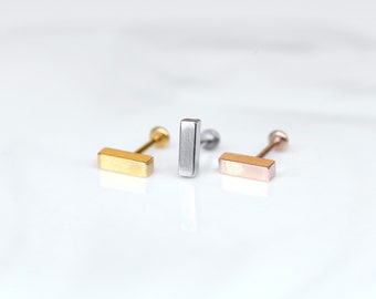 May include: Three bar-shaped earrings in gold, silver, and rose gold. Each earring has a small post and a ball at the end.