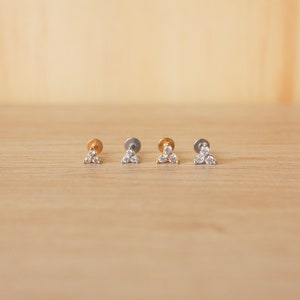 Op de afbeelding: Vier kleine driehoekige oorringen met elk drie heldere zirkonia-stenen. Twee oorringen zijn goudkleurig en twee zijn zilverkleurig.