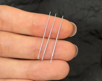 May include: Three silver metal needles, held in a hand, are used for crafting and sewing.