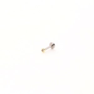 May include: A single, silver-colored labret stud with a small, round, gold-colored bezel setting a tiny, clear gemstone. The stud has a flat back and a ball end. The jewelry is set against a white background.