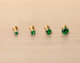 May include: Four gold nose rings with green gemstones of varying sizes. The rings are arranged in a row from smallest to largest.