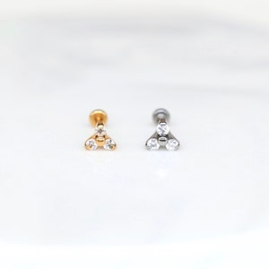 Op de afbeelding: Twee lichaamssieraden van chirurgisch staal met een driehoek van heldere zirkonia-stenen. Een stuk is goud en het andere is zilver.