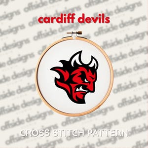 Può includere: Un modello a punto croce in un telaio di legno. Il disegno presenta una testa di diavolo rossa e nera con il testo "Cardiff Devils" e "CROSS STITCH PATTERN".