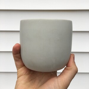 May include: A light gray concrete planter with a rounded bottom and a smooth, matte finish.