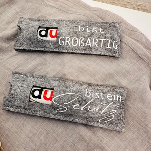 Puede incluir: Dos bolsas de regalo de fieltro gris con letras blancas. La bolsa superior dice "Du bist gro&szlig;artig" y la bolsa inferior dice "Du bist ein Schatz".