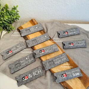 Puede incluir: Un conjunto de diez etiquetas de regalo de fieltro gris con texto blanco. Cada etiqueta tiene un mensaje diferente, incluyendo "Eres incre&iacute;ble", "Eres maravilloso", "Eres un tesoro", "Eres &uacute;nico", "Eres especial", "Eres amado", "Eres apreciado", "Eres importante", "Eres valioso" y "Eres irremplazable".