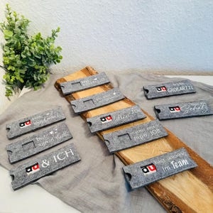 Puede incluir: Un conjunto de diez cajas de regalo de fieltro gris con texto blanco y un logotipo rojo. El texto en las cajas incluye "Eres incre&iacute;ble", "Eres maravilloso", "Eres una gran persona", "Haces un gran trabajo", "Haces un gran trabajo", "Haces un gran trabajo", "Haces un gran trabajo", "Haces un gran trabajo", "Haces un gran trabajo", "Haces un gran trabajo".