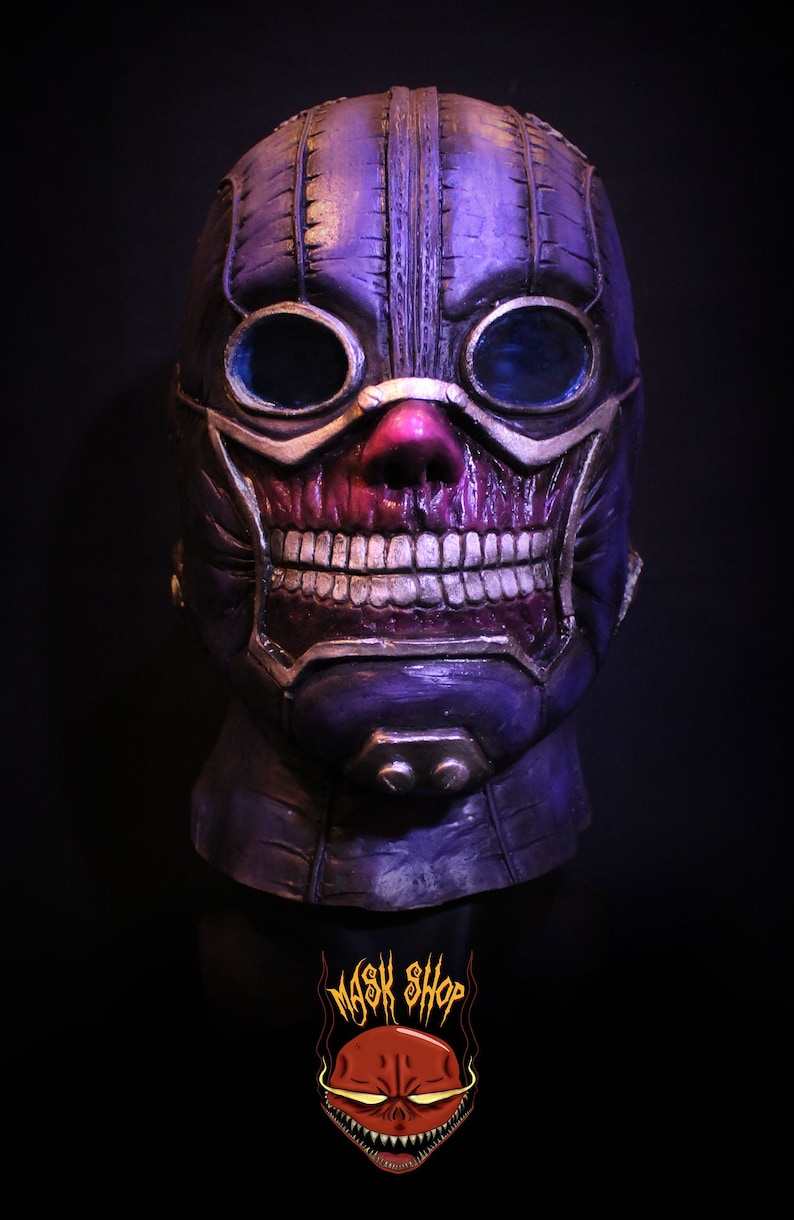 Pu&ograve; includere: Una maschera di teschio viola e oro con occhiali. La maschera ha un design cucito e un viso di teschio dettagliato con denti.