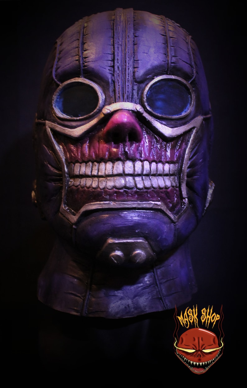 Pu&ograve; includere: Una maschera di teschio viola e argento con occhiali. La maschera ha un design cucito e un viso di teschio dettagliato con i denti. La maschera &egrave; su uno sfondo nero.