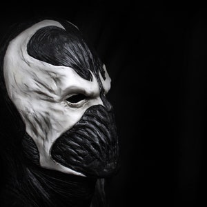 May include: A black and white mask with a detailed design. The mask has a sharp, angular shape and a single eye hole. The mask is made of a smooth, textured material.