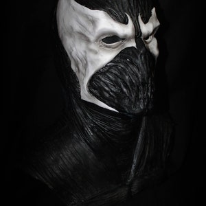 May include: A black and white latex mask of a character with a skull-like face and a white, textured, skull-like design on the forehead. The mask is a full-face mask and covers the entire head. The mask is made of latex and has a realistic look.