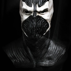 Può includere: Una maschera in lattice bianco e nero di un personaggio di supereroe con un viso a forma di teschio. La maschera ha una superficie testurizzata e uno schema di colori bianco e nero. La maschera è un personaggio popolare dei fumetti e dei film.