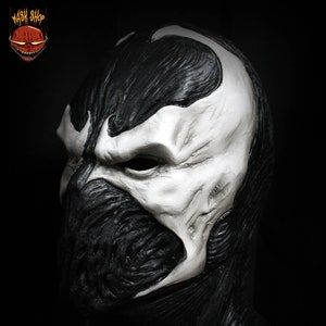 May include: A black and white latex mask of a character with a skull-like face. The mask has a detailed, textured surface and a white skull-like face with a black mouth and eyes.